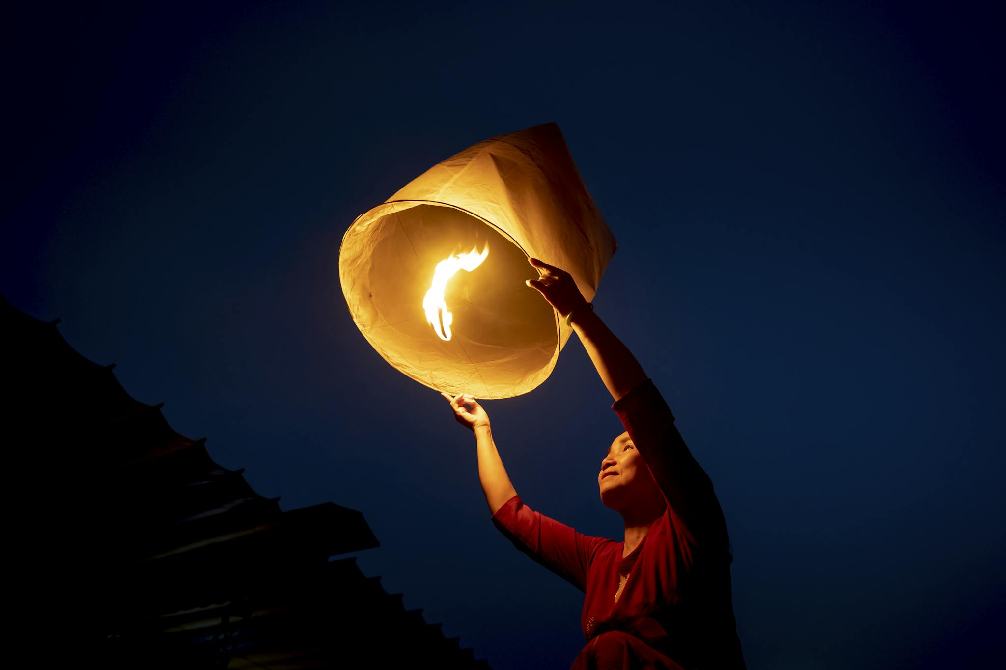 A person releasing a glowing sky lantern against a dark night sky.
