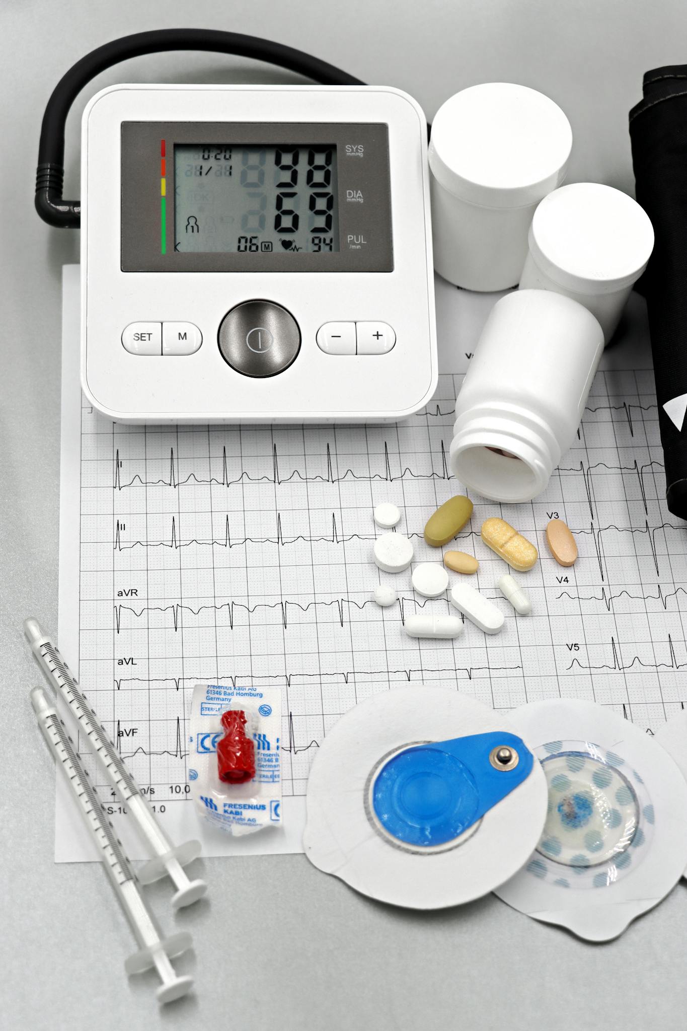 Medical setup featuring blood pressure monitor, pills, syringes, and ECG printout for healthcare themes.